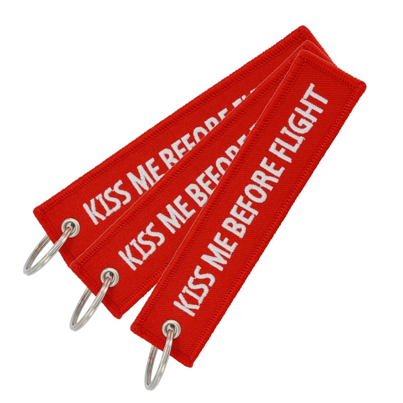 Red woven keychain with the text Kiss Me Before Flight