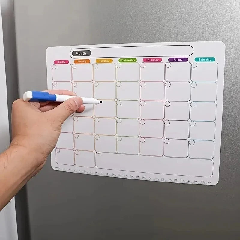 A hand writes on a magnetic fridge planner grid showing monthly days and space for notes.