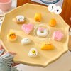 A hand holds a yellow silicone food mold tray filled with various cute cartoon-themed food shapes like fruits and pastries.