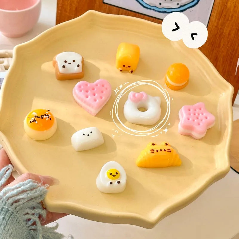 A hand holds a yellow silicone food mold tray filled with various cute cartoon-themed food shapes like fruits and pastries.