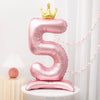 A pink foil balloon shaped like the number five with a gold crown on top