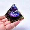 A hand holds a clear pyramid crystal with purple and gold decorative elements representing twelve zodiac signs.