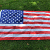 A large American flag made of double-sided polyester spread out on green grass.