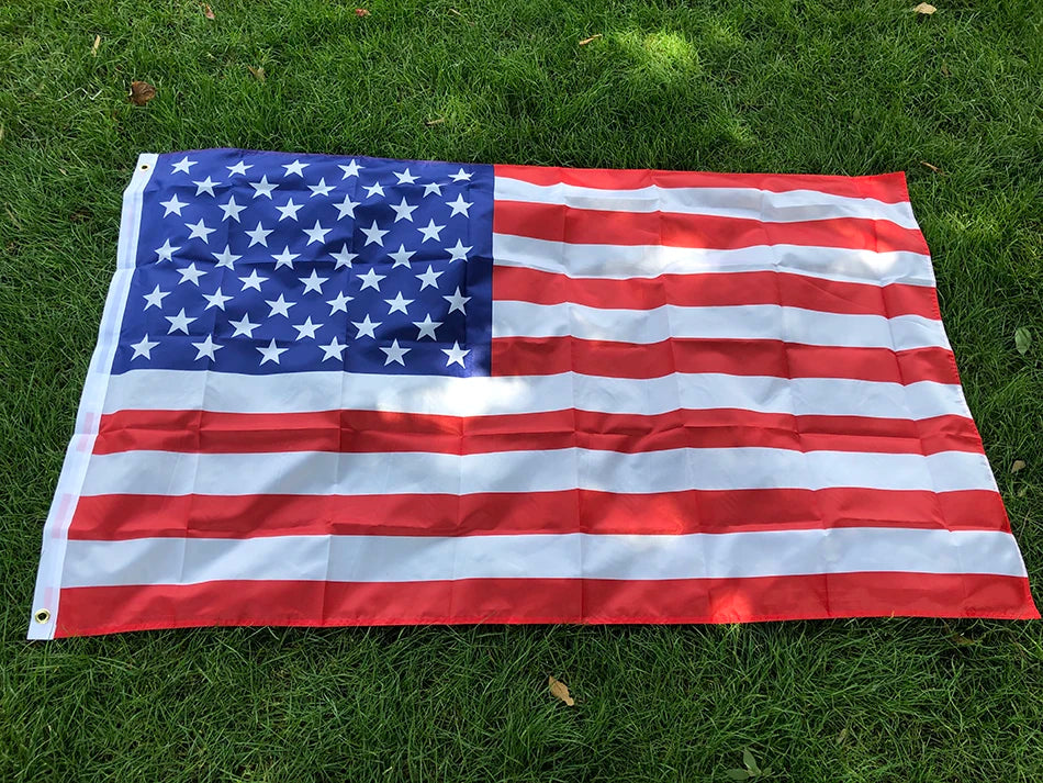 A large American flag made of double-sided polyester spread out on green grass.