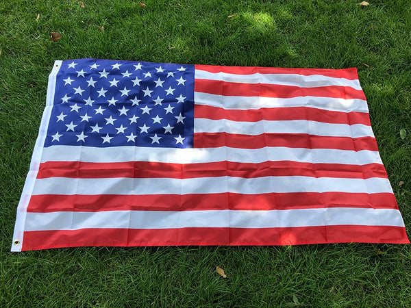 A large American flag made of double-sided polyester spread out on green grass.