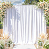 A white fabric backdrop with vertical pleats and floral greenery used as an event decoration.