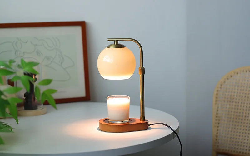 A brass aromatherapy wax melting lamp with a frosted glass shade and a candle sits on a white table.