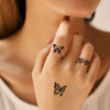 A close-up of a woman's hand showing realistic black butterfly temporary tattoos on her finger.