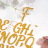 A hand holds a white sticker with a gold glitter letter F above a sheet of gold glitter alphabet letters.