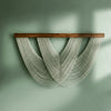Bohemian macrame wall tapestry featuring white cord hanging from a wooden bar against a muted green wall.