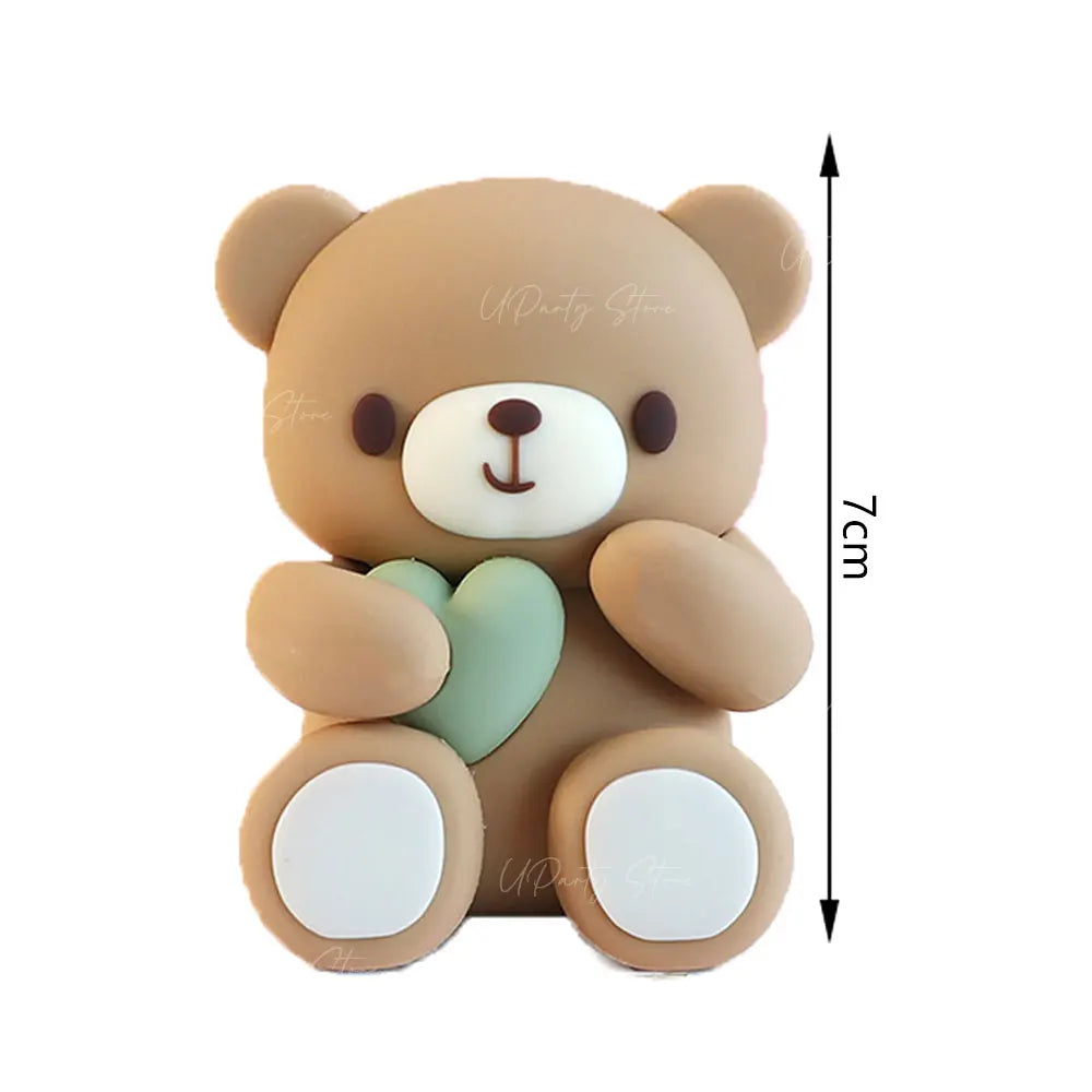 A cute brown teddy bear shaped cake topper with pink ball decorations and a measuring scale.