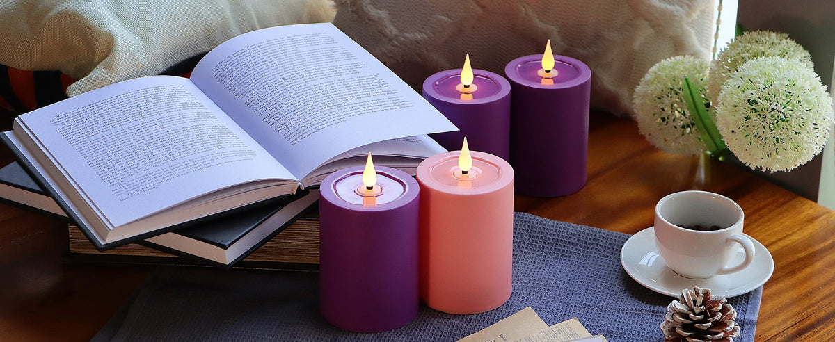 A collection of purple and coral flameless LED candles with wicks, an open book, and pine cones on a wooden surface.
