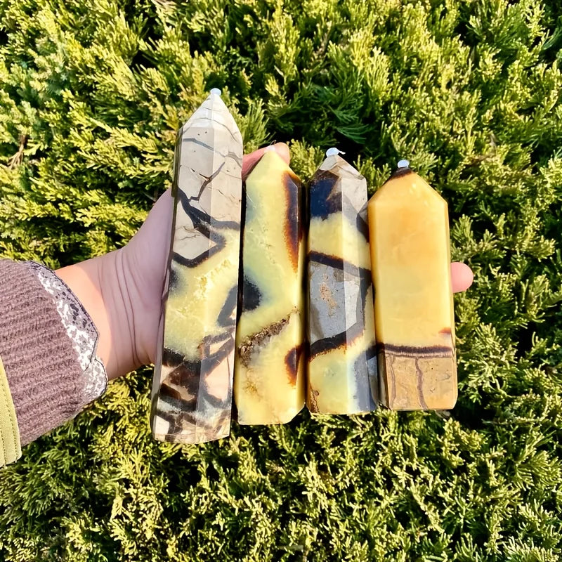Une main tient quatre tours de cristaux naturels avec des veines jaunes et brunes sur un fond de mousse verte.