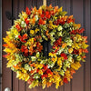 A circular wreath made of artificial autumn leaves in shades of red, orange, yellow, and green hanging on a dark wooden door.