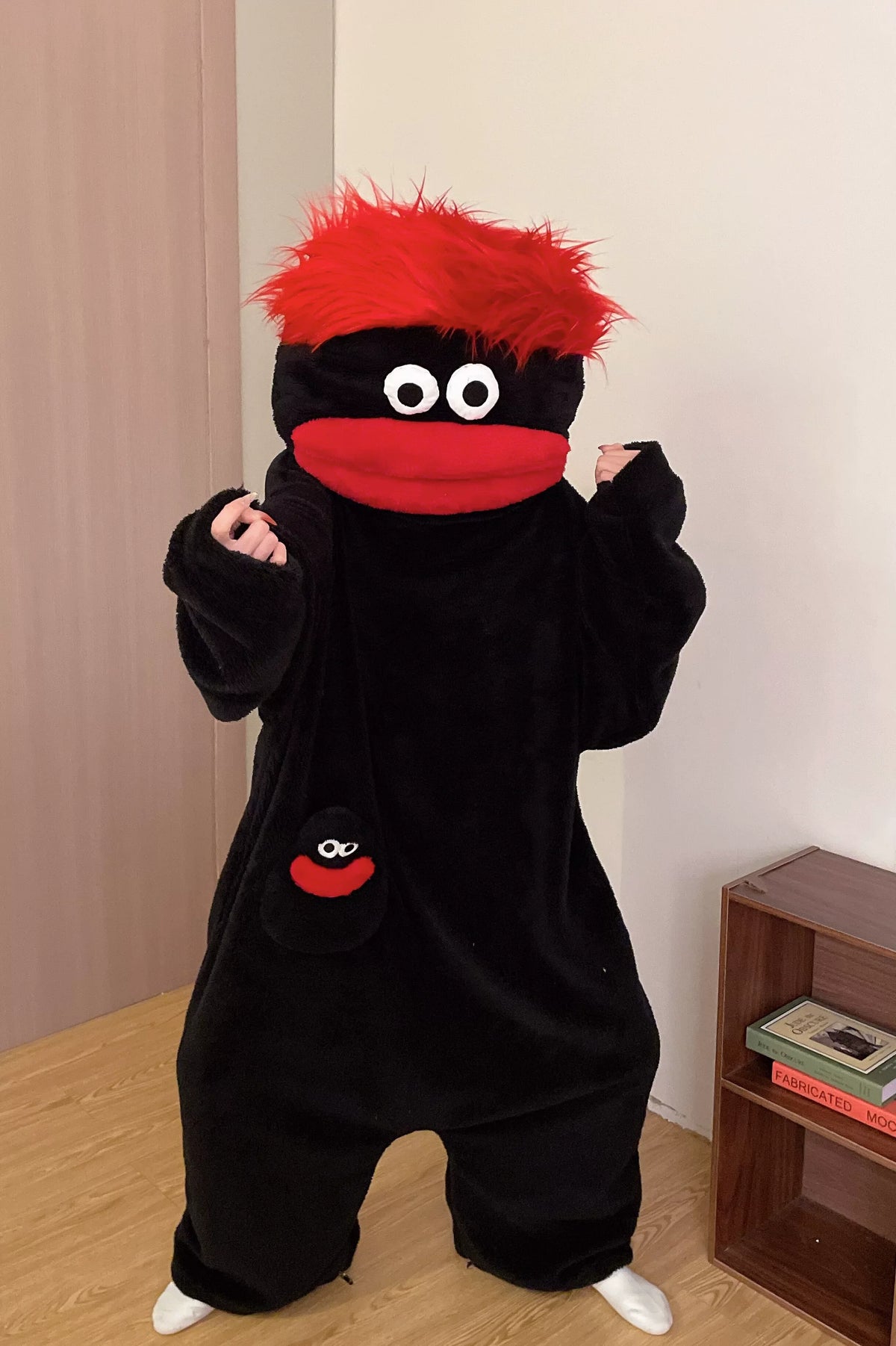A black monster onesie pajama suit with red accents is displayed on a light wooden floor.