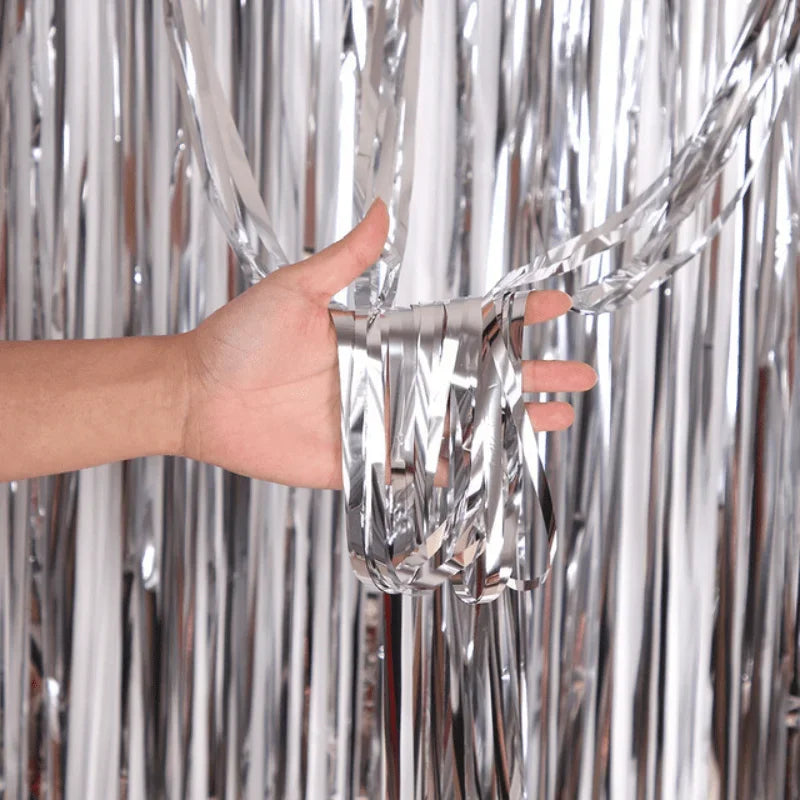 A hand is touching metallic silver foil fringe curtain material hanging vertically.