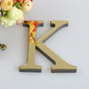 A gold letter K cutout for a mirror wall decal set placed next to a bouquet of yellow and pink roses.