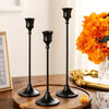 A set of three black ornate vintage metal candle holders displayed on a wooden surface.