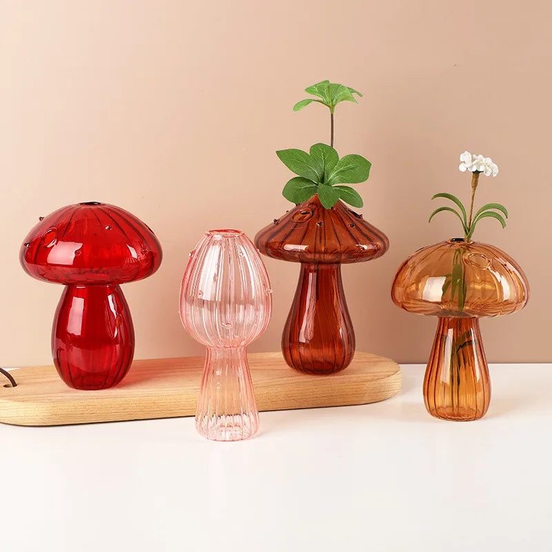 Three glass vases shaped like mushrooms in translucent red, pink, and amber tones with green leaves.