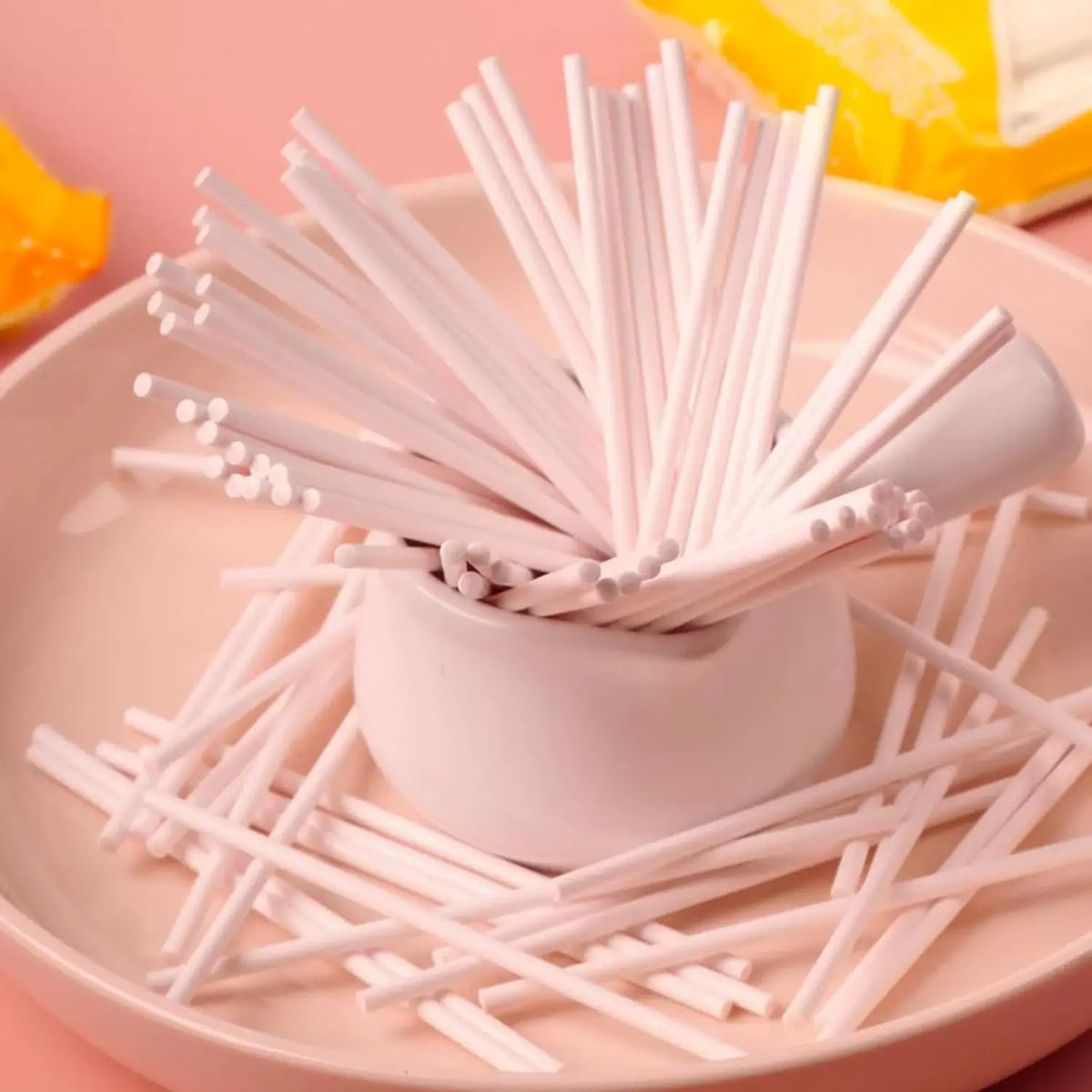 A pile of white paper lollipop sticks arranged on a pink plate.