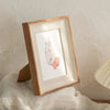 A wooden photo frame displaying a pink glass jar filled with pink liquid and rolled pink candies.