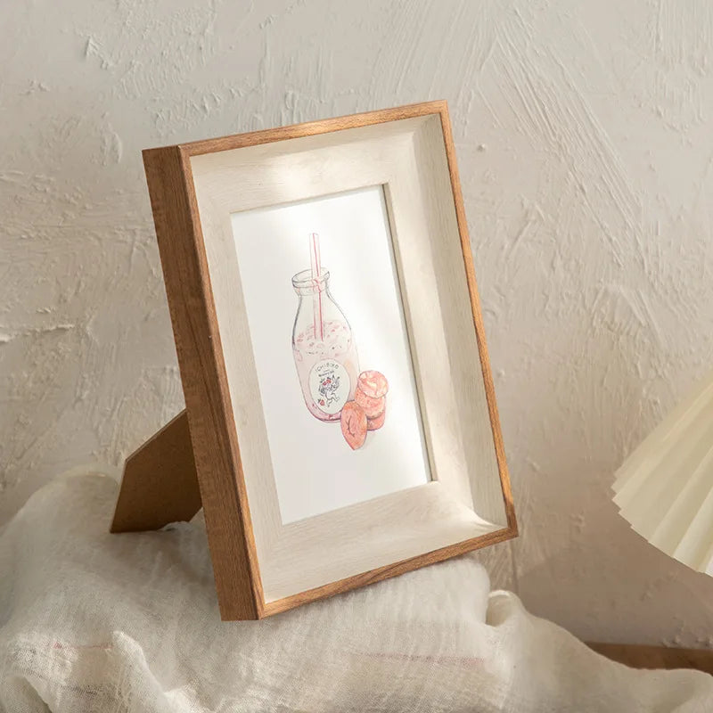 A wooden photo frame displaying a pink glass jar filled with pink liquid and rolled pink candies.