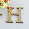 A gold letter H cutout for a mirror wall decal set placed next to a bouquet of flowers.