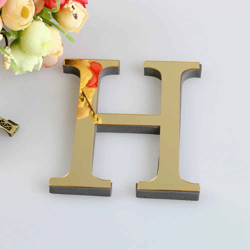 A gold letter H cutout for a mirror wall decal set placed next to a bouquet of flowers.