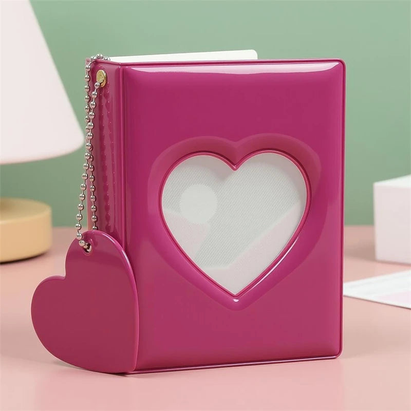 A pink candy heart window photocard album with a silver chain detail resting on a light pink surface.