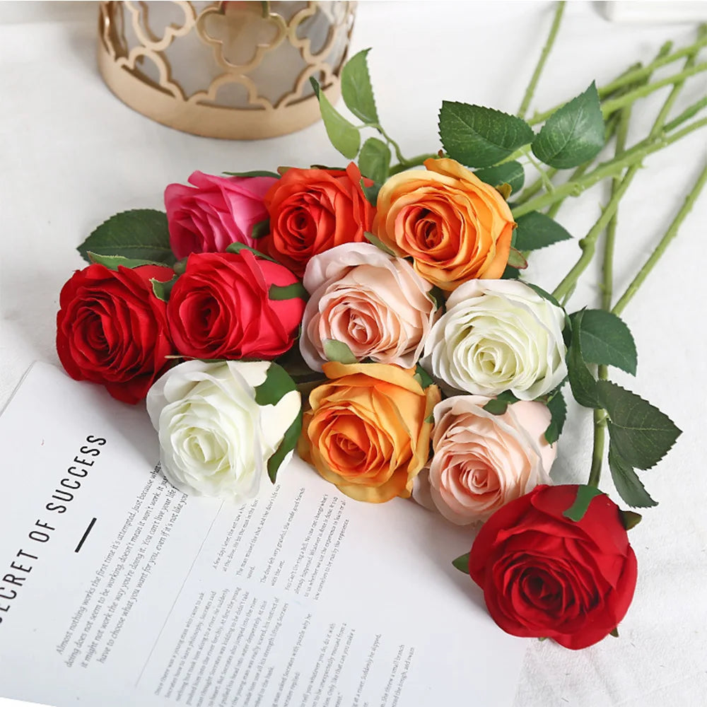 A bouquet of artificial roses in shades of red, pink, and orange arranged on a white surface.