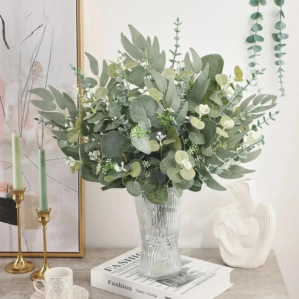 A bouquet of artificial eucalyptus leaves in various shades of green and white displayed in a glass vase.