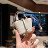 A hand holds a small, beige leather handbag with a blue patterned wrist strap.