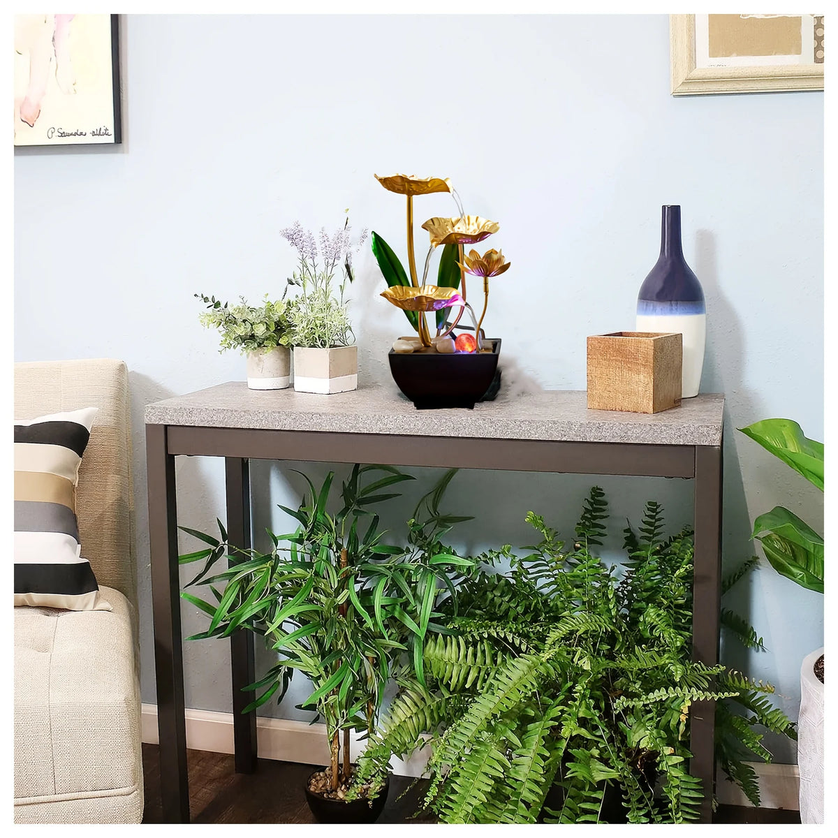 A potted plant and decorative items are displayed on a gray table with a large green fern in the foreground.