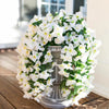 A lush white artificial bougainvillea vine garland arranged in a silver vase outdoors.