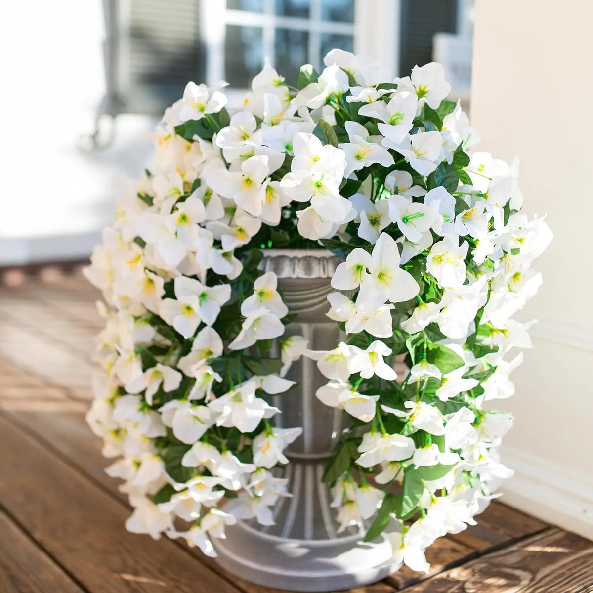 A lush white artificial bougainvillea vine garland arranged in a silver vase outdoors.
