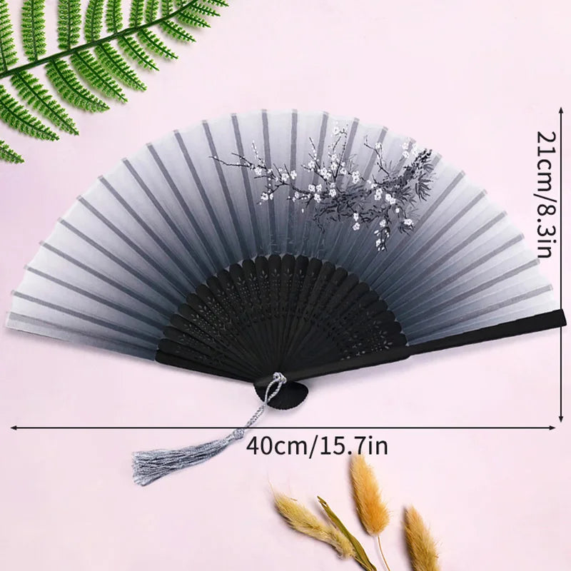 A gray and black elegant bamboo folding hand fan with a tassel displayed against a pink background.