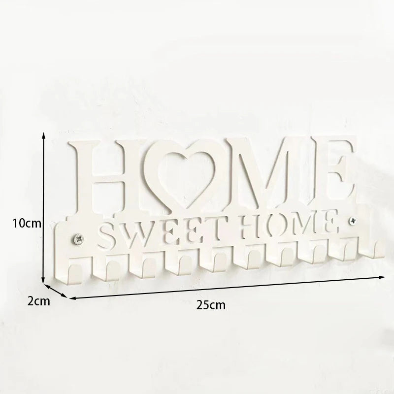 A white metal key holder with the words HOME SWEET HOME cut into the design, featuring wall-mounted hooks.