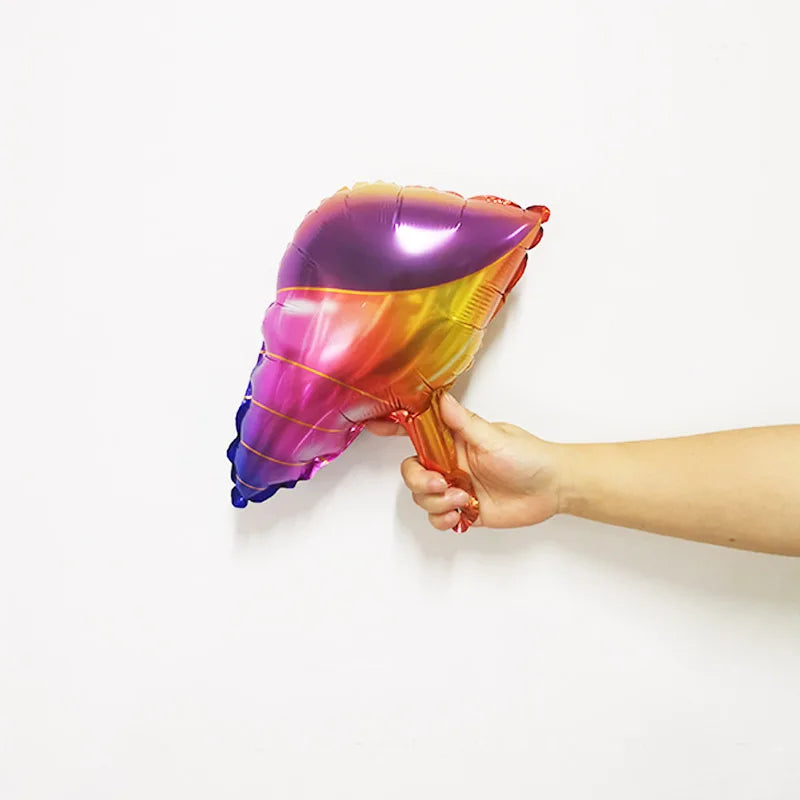 A hand holds a iridescent, foil balloon shaped like an ocean animal against a white background.