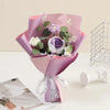 A bouquet of handmade crochet rose flowers in shades of purple and green, wrapped in pink paper.