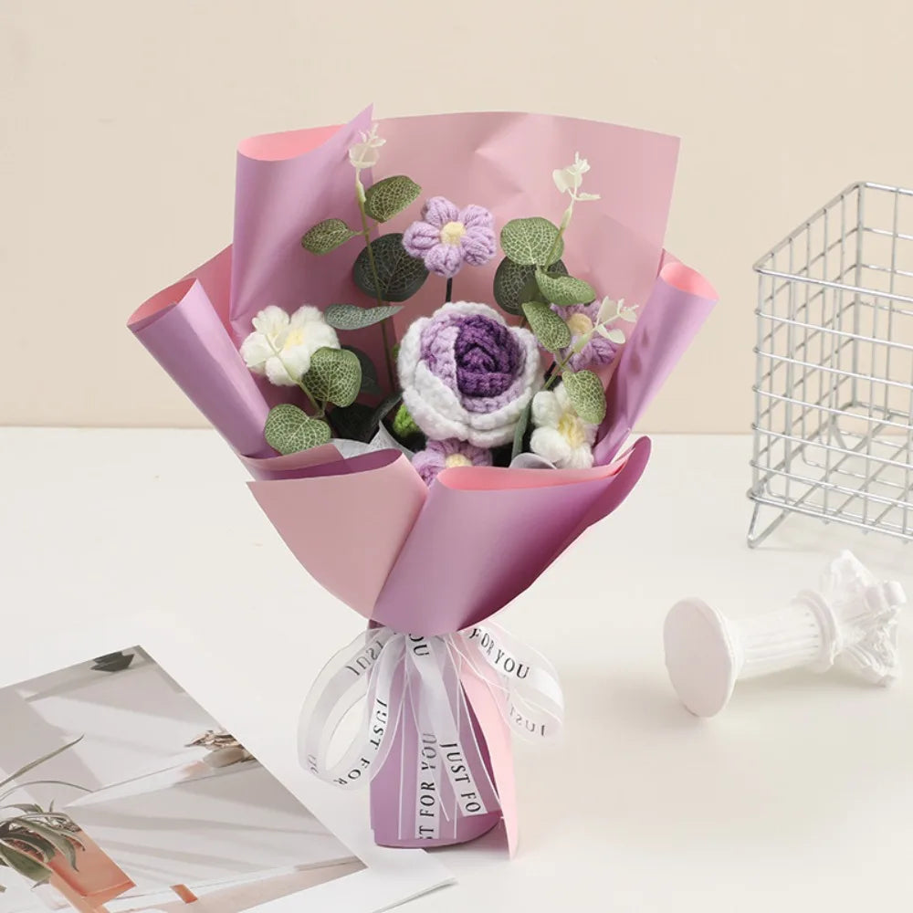 A bouquet of handmade crochet rose flowers in shades of purple and green, wrapped in pink paper.