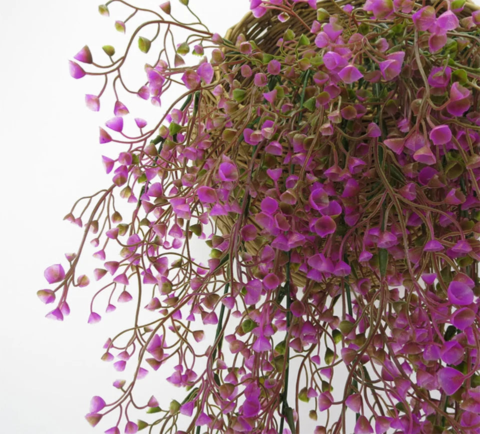 A close-up of artificial plant vines with small purple flowers and green leaves forming a hanging arrangement.