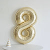 A large gold foil number balloon shaped like the number 8 is displayed on a white surface.