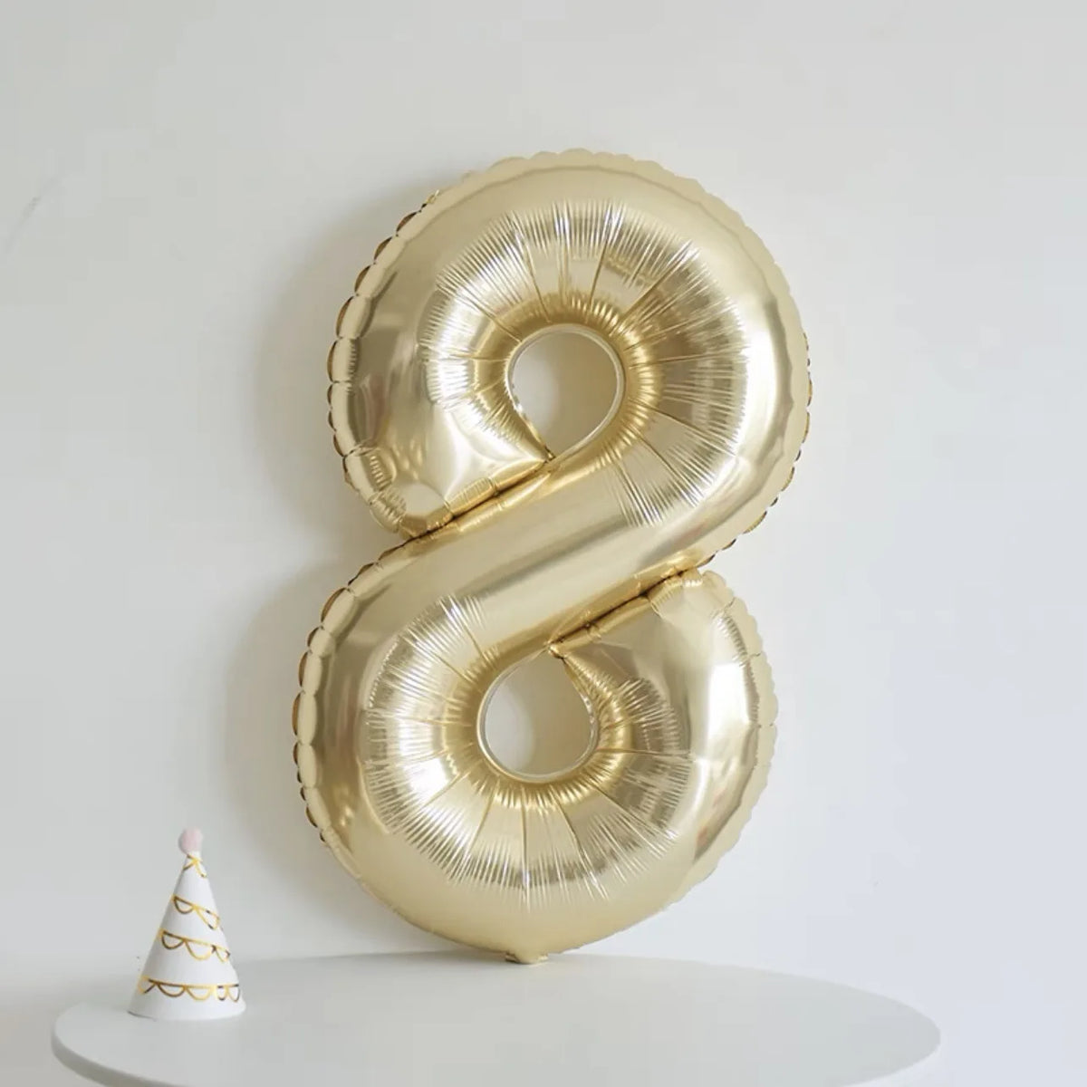 A large gold foil number balloon shaped like the number 8 is displayed on a white surface.