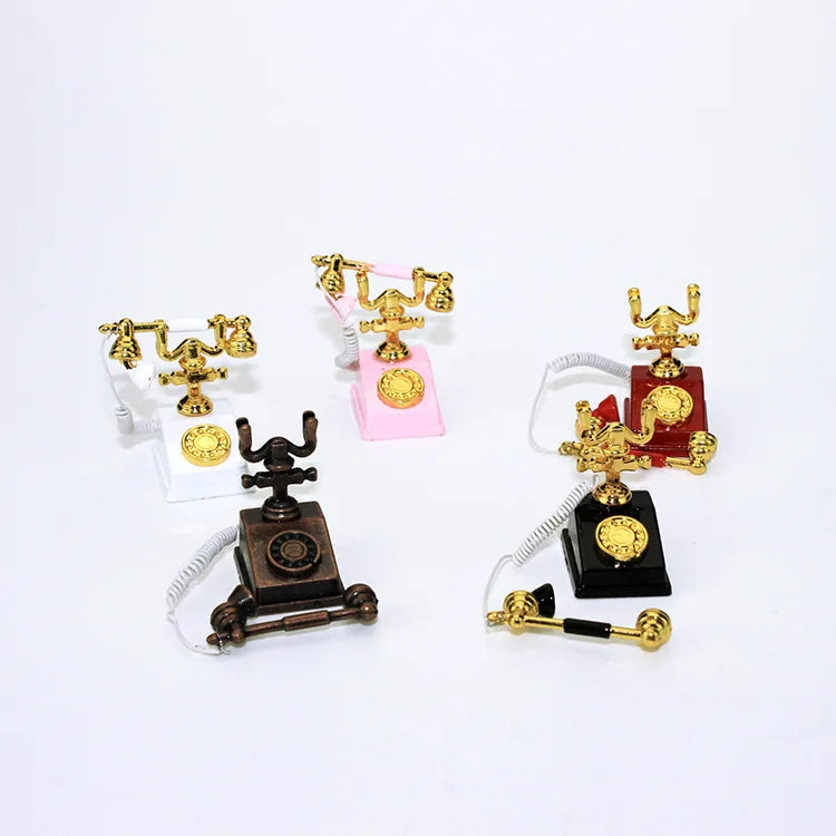 A collection of vintage rotary desk phone miniatures in gold and brass on pink, white, and black stands.