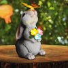 A gray rabbit statue with a butterfly perched on its nose, sitting on a wooden surface.