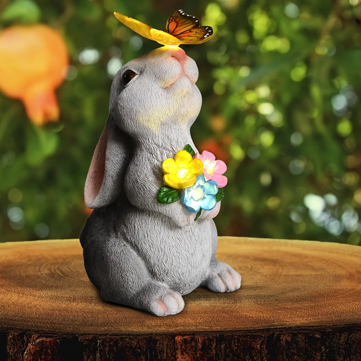 A gray rabbit statue with a butterfly perched on its nose, sitting on a wooden surface.