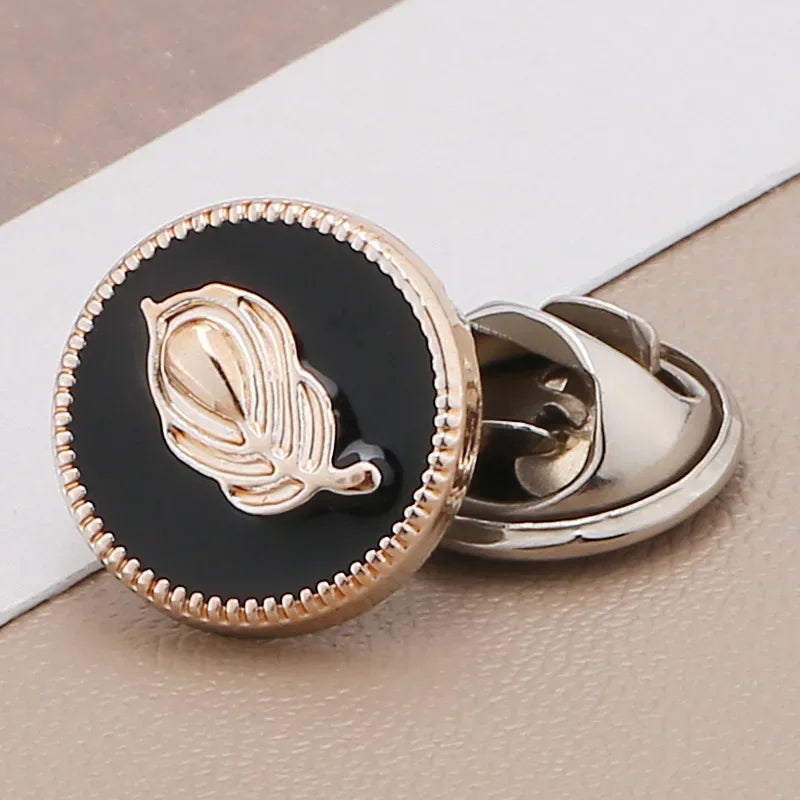 A close-up of a gold-toned no-sew brooch button featuring a silver-toned leaf design on a black background.