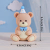 A cute, round beige bear baby block cake topper with a light blue bow and a small blue cone on top.