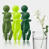 A set of three green and yellow human-shaped plant supports standing next to a glass of water.