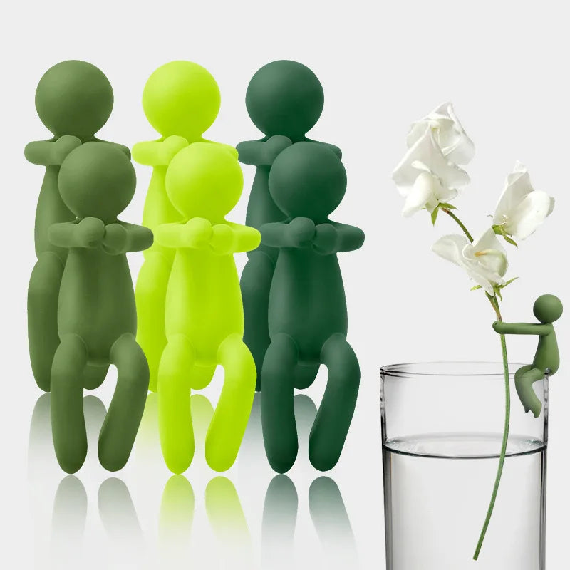 A set of three green and yellow human-shaped plant supports standing next to a glass of water.